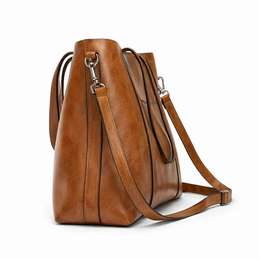 Bolso marrón visto de lado, con bandolera larga y herrajes metálicos
