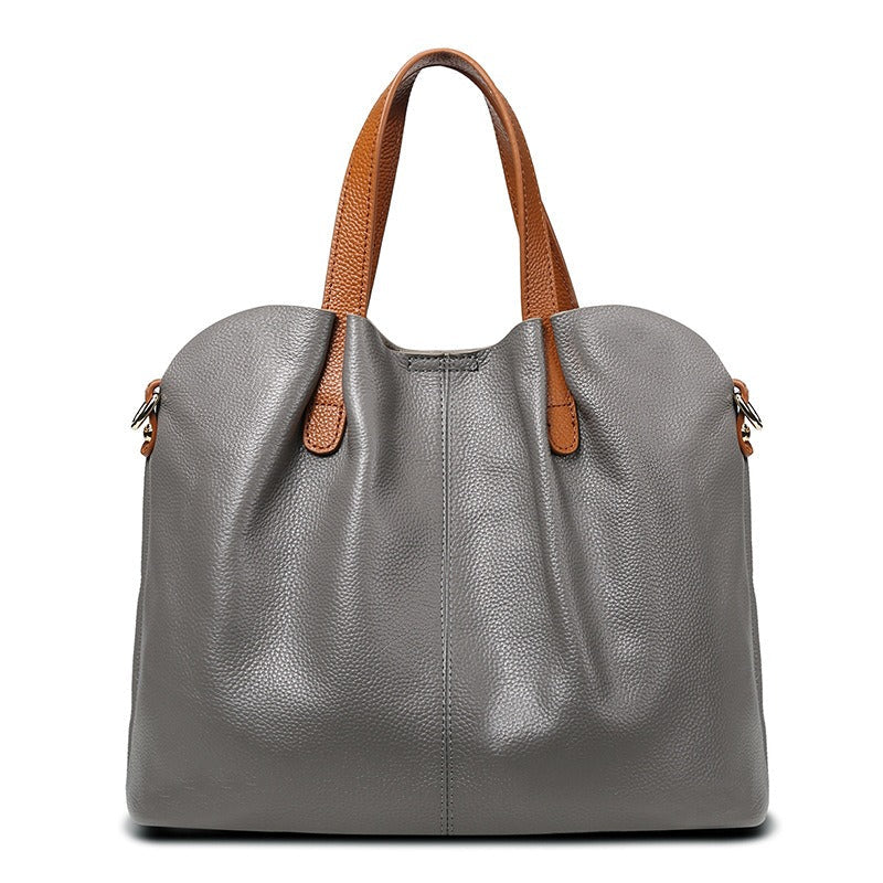 Bolso de mano gris con textura granulada, asas marrones y herrajes laterales