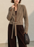 Cárdigan de punto beige con cuello alto, cremallera y lazadas amplias en la cintura