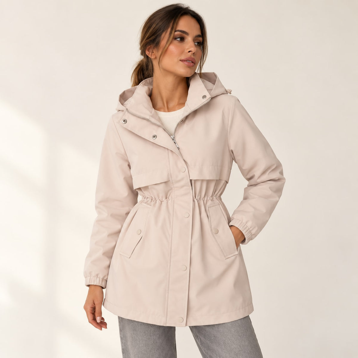 Parka beige con capucha, bolsillos tipo parche y cintura fruncida ajustable.