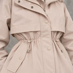 Parka beige con cordones en la cintura, botones a presión y detalle de trabillas.