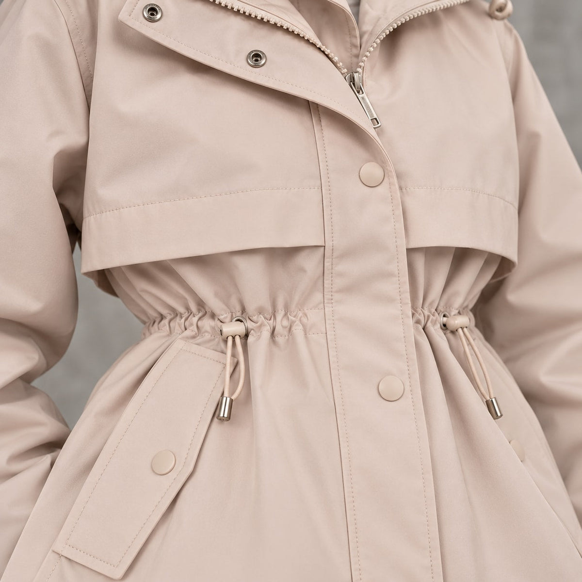 Parka beige con cordones en la cintura, botones a presión y detalle de trabillas.