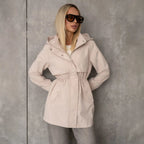 Parka beige con capucha y cintura ajustable, bolsillos laterales y cierre frontal.