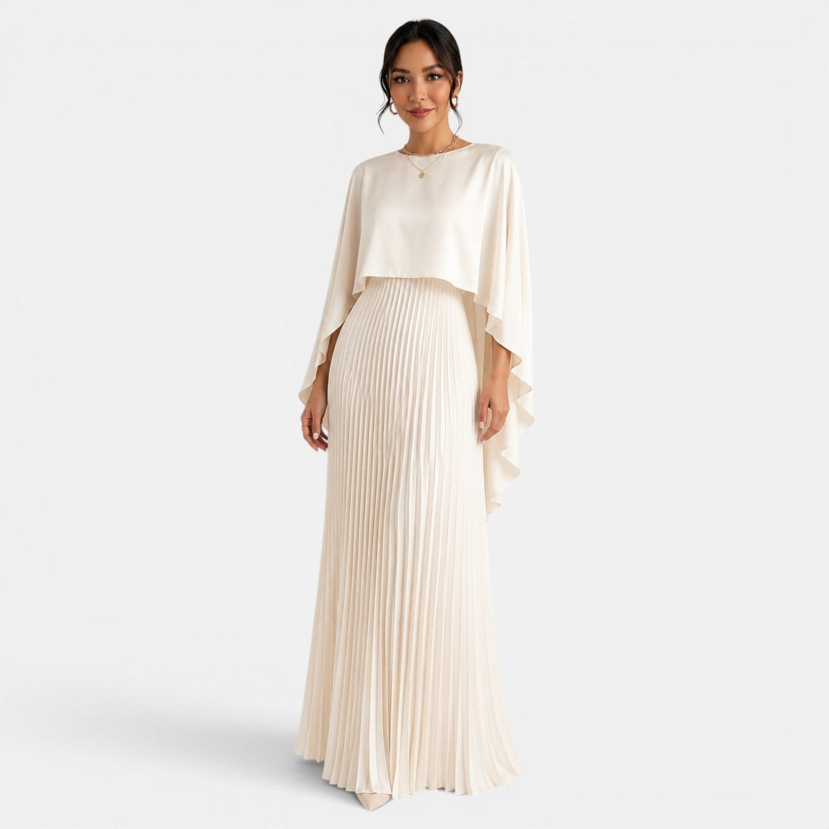 Vestido largo beige con falda plisada y capa asimétrica de mangas murciélago, vista frontal.