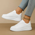 Zapatillas de piel blancas de caña baja con cordones y suela gruesa; tobillo con pulsera dorada